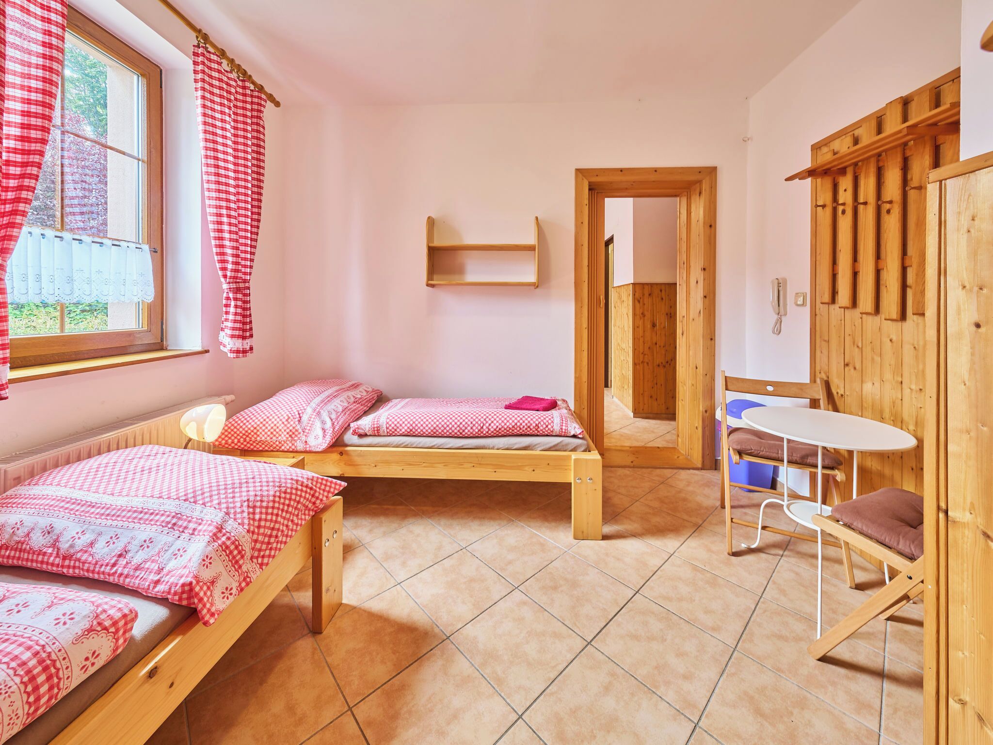 A room with two wooden beds, a small table, a chair, and a wooden wardrobe.