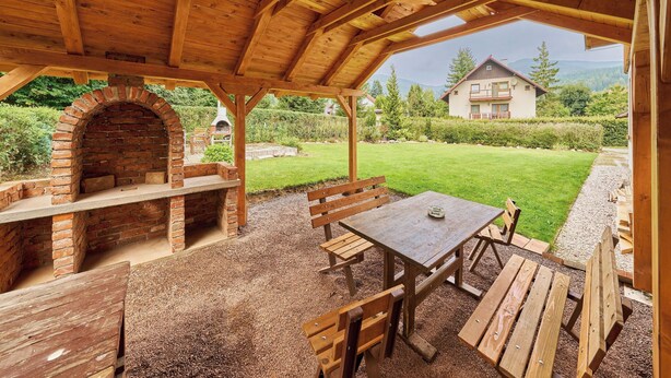An outdoor wooden pavilion with a brick oven, picnic tables, and benches.