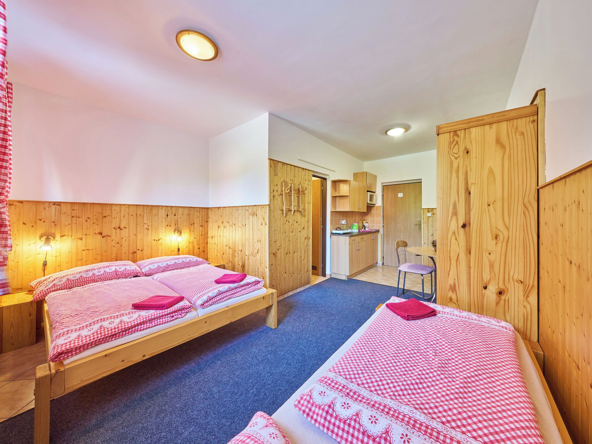 Een kamer met twee houten bedden, een kitchenette en een badkamer die door een open deur zichtbaar is.