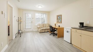 Ein kompakter Wohnraum mit Küchenzeile, einer Couch, einem Schreibtisch und einer Kaffeemaschine.