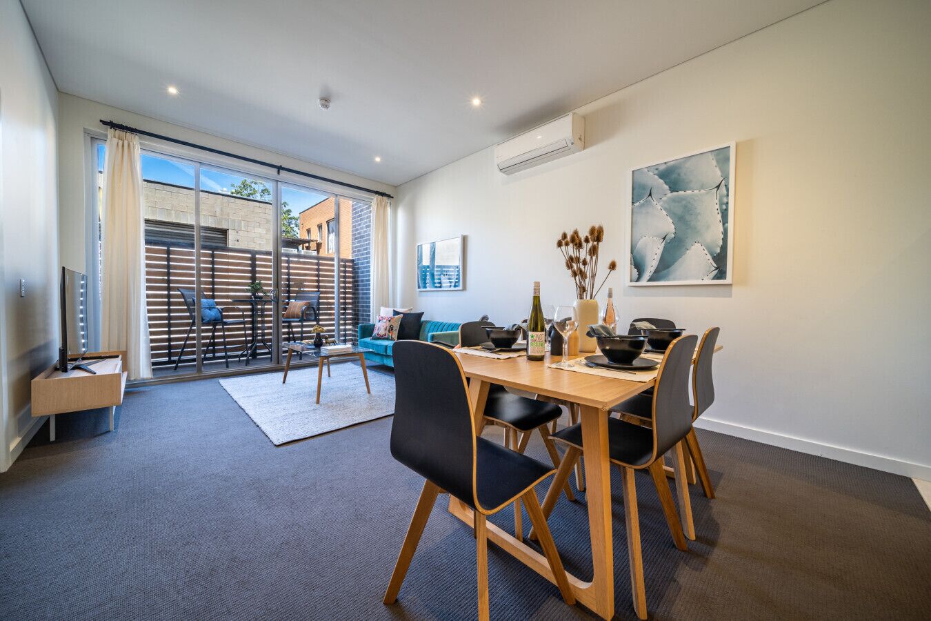 A modern dining area with a wooden table, black chairs, and a blue sofa in the background.