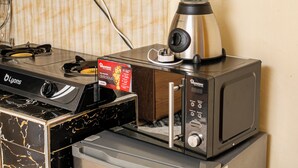 A kitchen with a blender on top of a microwave, a stove, and a box of food. - FURNISHED COZY ONE BEDROOM APARTMENT (Busia)