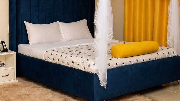 A bed with a blue headboard, white bedding, and a yellow pillow. - FURNISHED COZY ONE BEDROOM APARTMENT (Busia)