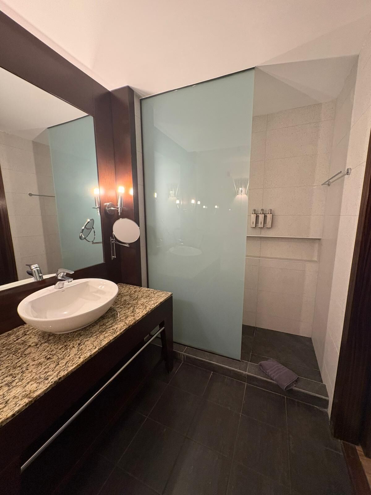 A modern bathroom with a granite countertop, a white sink, and a glass shower enclosure.
