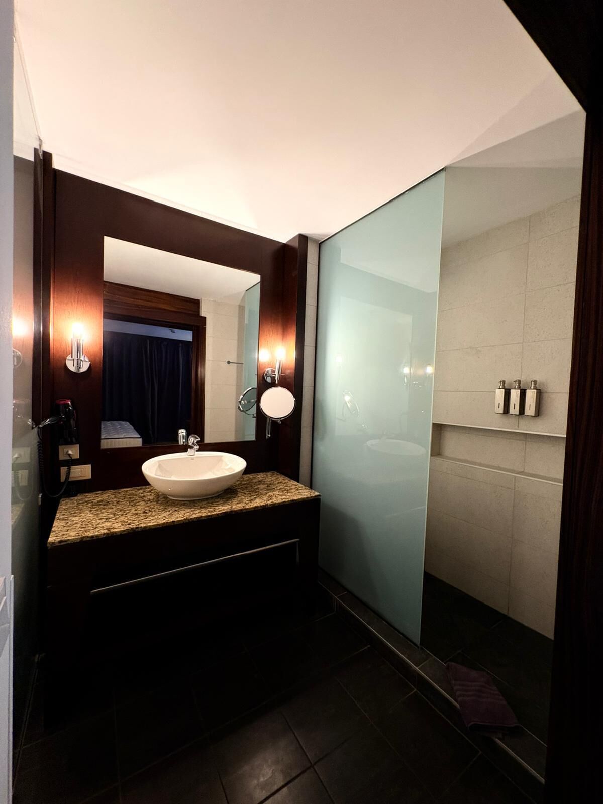 Een moderne badkamer met een wastafel met granieten blad, een grote spiegel en een douche met glazen wanden.