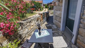 A stone-walled outdoor seating area with a table and chairs, a bottle of wine, and a glass. - Vacation home Petra by Interhome (Umag)