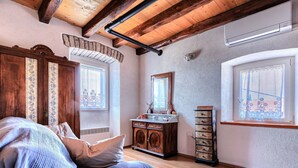 A room with a bed, wooden beams, a dresser, a mirror, and two windows with lace curtains. - Vacation home Petra by Interhome (Umag)