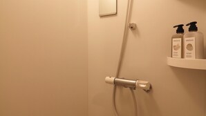A bathroom with a shower, a light fixture, and a shelf with two bottles.