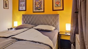 Ein Bett mit Decke, zwei Nachttische mit Lampen und drei gerahmte Kunstwerke an der Wand.