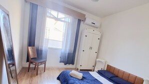 A bedroom with a bed, a chair, a wardrobe, and a window with curtains.