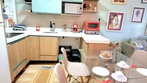 A compact kitchen with wooden cabinets, a microwave, and a dining area with a glass table and chairs.