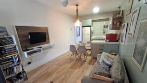 A compact living space with a sofa, a dining table with chairs, a TV mounted on the wall, and a bookshelf.
