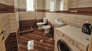 A bathroom with a shower, toilet, bidet, sink, and a washing machine. - Albania Dream Saranda Apartments (Saranda)
