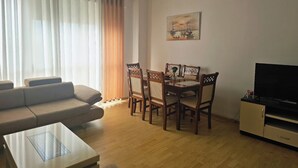 A living room with a sofa, dining table, chairs, a coffee table, and a TV. - Albania Dream Saranda Apartments (Saranda)