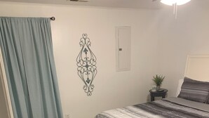 A bedroom with a bed, a blue curtain, a decorative wall piece, a small potted plant, and a gray and white striped bedspread. - Spacious 4-bedroom apartment with WiFi, AC in charming Conway (Conway)