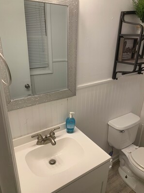 A bathroom with a white sink, a mirror with a mosaic frame, a toilet, and a shelf with a plant.