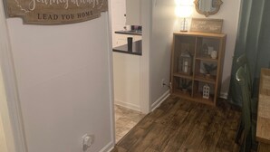 A hallway with a wooden sign saying "May your journey always lead you home," a mirror, a shelf with decorative items, and a door leading to a kitchen area. - Spacious 4-bedroom apartment with WiFi, AC in charming Conway (Conway)