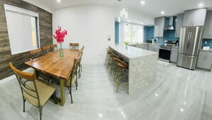 A modern kitchen with a wooden dining table, bar stools, and a central island. - Charming Villa with Pool and Lake View (Miramar)