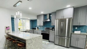 A modern kitchen with granite countertops, stainless steel appliances, and a central island with bar stools. - Charming Villa with Pool and Lake View (Miramar)