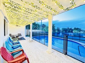 Un espacio al aire libre techado con piscina, sillas y vista al océano.