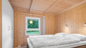 Une chambre avec un plafond en bois, un lit recouvert de draps blancs et une fenêtre donnant sur un paysage verdoyant.