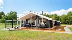 Une maison moderne dotée d’une grande terrasse, d’un espace salon extérieur et d’une véranda en verre.