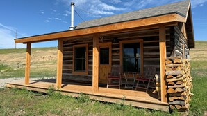 A log cabin with a porch, stone wall, and a chimney.