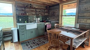A rustic kitchen with wooden beams, a dining table, and a view of the outdoors.