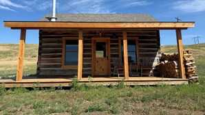 A log cabin with a wooden porch, a chimney, and a stack of firewood outside.