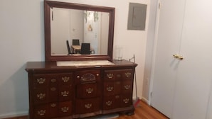 Une commode en bois avec un miroir, une porte et un interrupteur sur le mur.