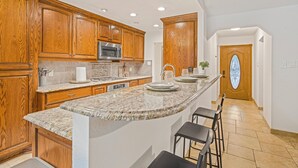 A kitchen with wooden cabinets, granite countertops, a built-in microwave, and a large island with bar stools. - Austin Escape w/ Pool, Hot Tub & Game Room – DT ,Bars, South Congress, Airport ! (Austin)