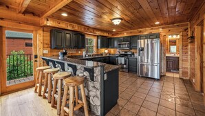 A kitchen with wooden cabinets, a central island with stools, a refrigerator, and a stove. - NEW 6BR: Sleep 22| Pool| Views| Cinema| Hot Tub| A+ Location| Dog Friendly (Sevierville)