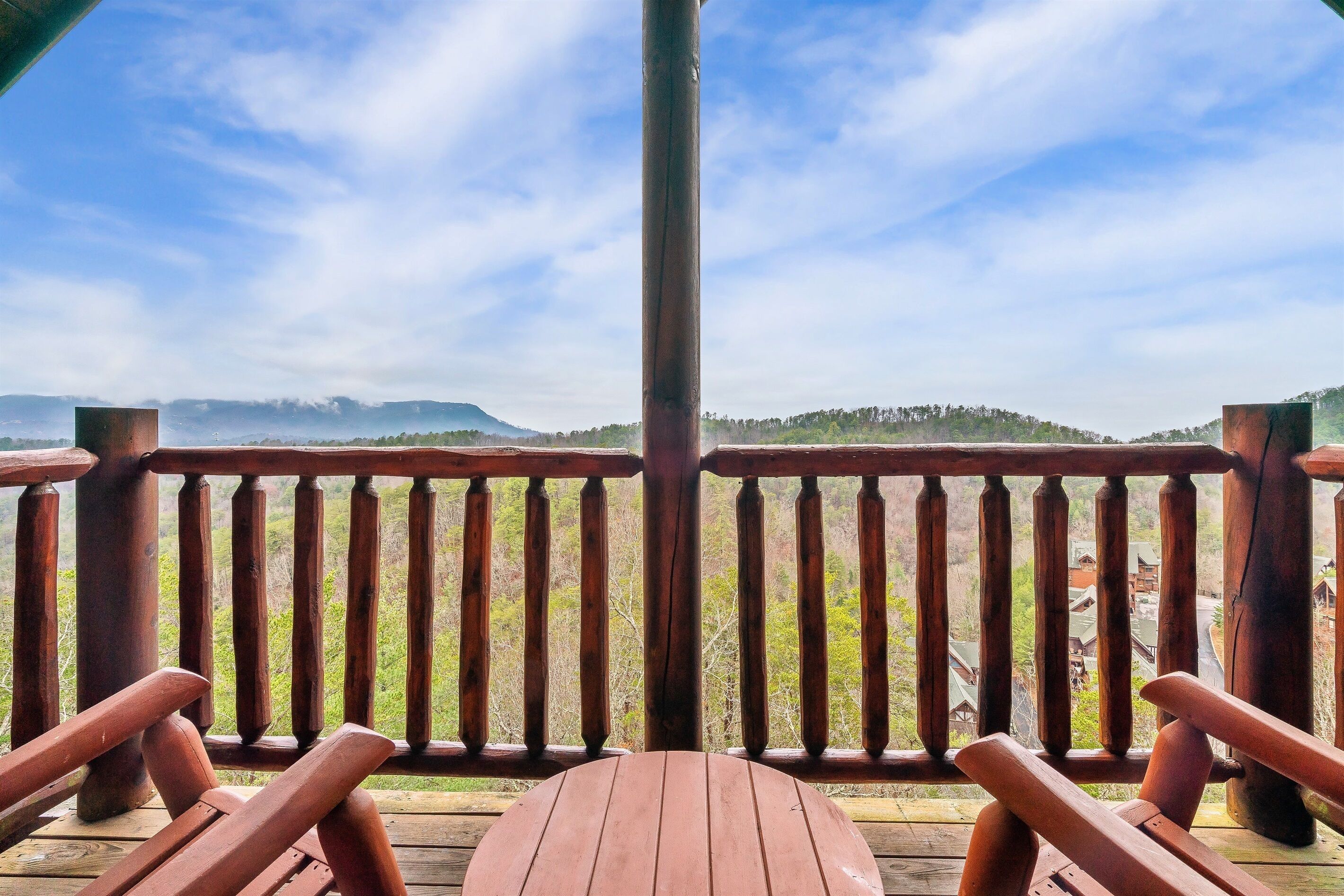 Une terrasse en bois avec une table et des chaises, offrant une vue sur un paysage montagneux sous un ciel dégagé.
