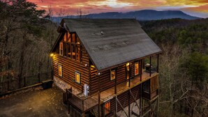 A wooden cabin with a balcony, surrounded by trees, and set against a sunset sky. - NEW 6BR: Sleep 22| Pool| Views| Cinema| Hot Tub| A+ Location| Dog Friendly (Sevierville)