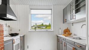 Eine Küche mit weißem Holzvertäfelung, einem Fenster mit Blick, einem Herd und grauen Schränken.