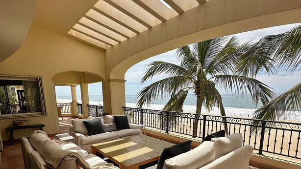 A spacious balcony with a view of the ocean, furnished with a sofa, a coffee table, and a TV.