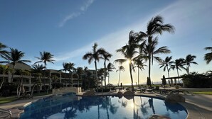 A swimming pool with clear blue water, surrounded by palm trees and a building with balconies.