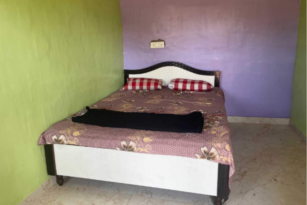 A single bed with a floral bedspread, two red and white checkered pillows, and a black throw blanket.