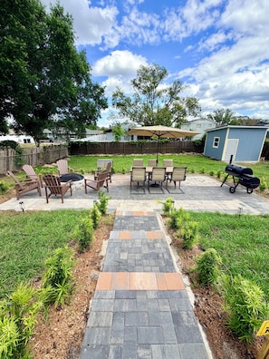 Un patio trasero con un sendero de piedra, muebles de exterior y una parrilla de barbacoa.