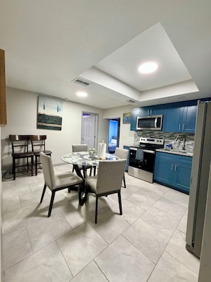 Una cocina moderna con armarios azules, un refrigerador de acero inoxidable y un comedor con mesa y sillas de vidrio.