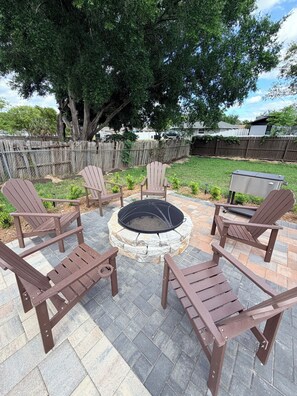 A patio with Adirondack chairs arranged around a stone fire pit. - Haven Retreat-Universal (Orlando)