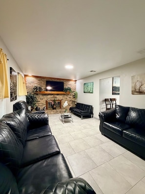 A living room with a brick fireplace, black leather sofas, a coffee table, and a flat-screen TV mounted on the wall.