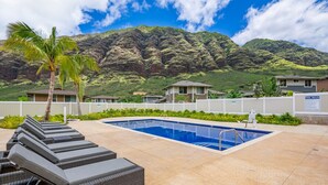 A swimming pool with lounge chairs and a palm tree, surrounded by a mountainous landscape. - Ocean + Mountain Views|Beach 6 Min|Fire Pit|Gated (Waianae)