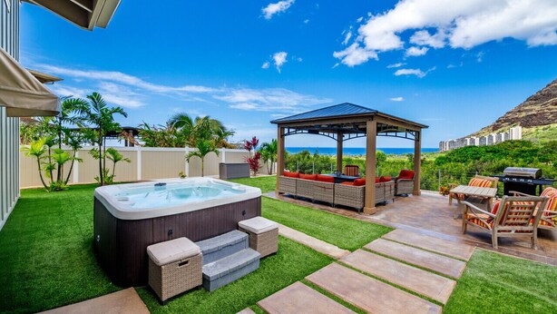 A backyard with a hot tub, outdoor seating, and a pergola overlooking a scenic view. - Ocean + Mountain Views|Beach 6 Min|Fire Pit|Gated (Waianae)