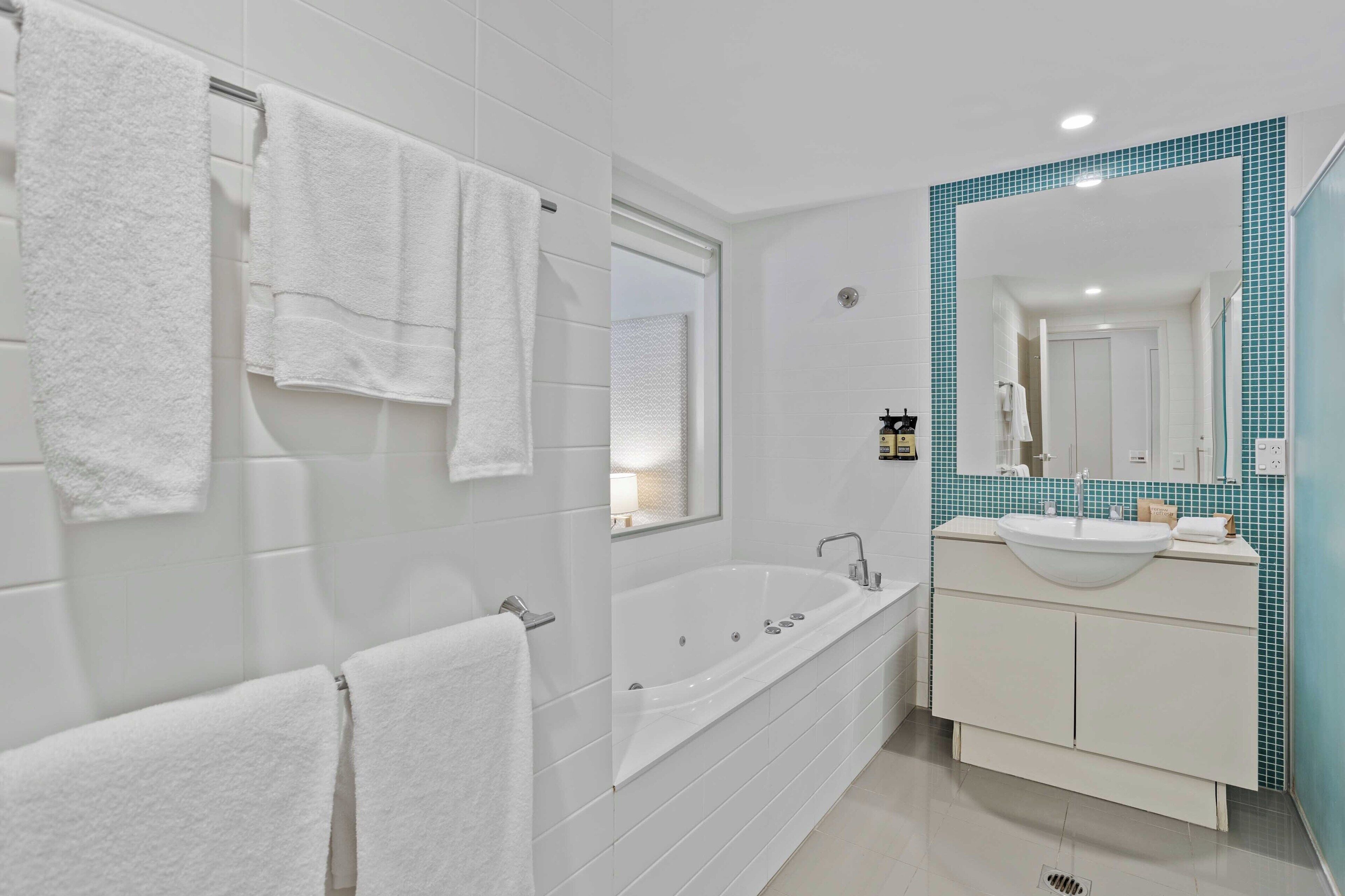 Un bany modern amb banyera, un mirall gran i un lavabo amb rentapelats.