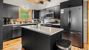 A modern kitchen with dark cabinetry, stainless steel appliances, and a wooden ceiling.