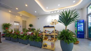 A modern lobby with a reception desk, a vending machine, and various potted plants.