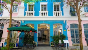 A colorful building with a blue and pink facade, a covered outdoor seating area with chairs and tables, and a sign indicating a restaurant or cafe.