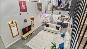 Un vaste espace de vie comprenant un grand canapé blanc, un téléviseur et un coin repas avec une petite table et des chaises.