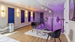 Une chambre moderne avec un plancher en bois, un lit, un bureau et une chaise. Un mur violet est décoré d’œuvres d’art encadrées, et le plafond est doté d’un éclairage encastré.